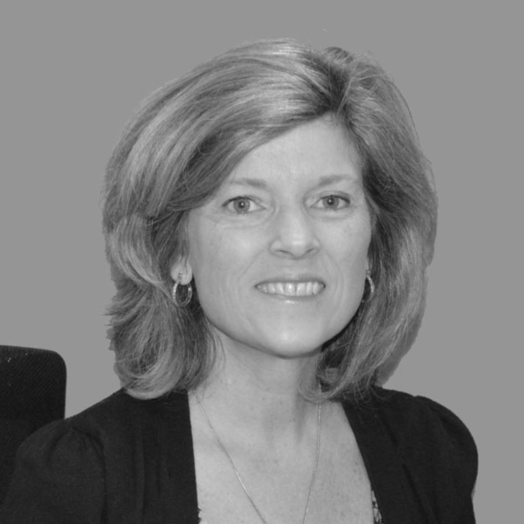 A woman with shoulder-length hair wearing hoop earrings and a dark top smiles at the camera. The background is a neutral grey.